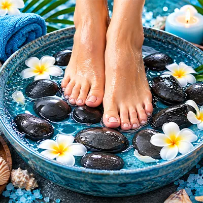Feet receiving a hot stone spa treatment surrounded by flowers and stones.
