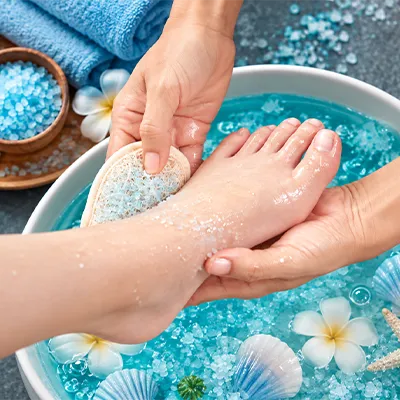 Feet soaking in a sea salt foot bath with blue water and spa stones.